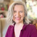 Lynn D. Warner, who is an ADHD Coach smiles wearing a purple shirt.